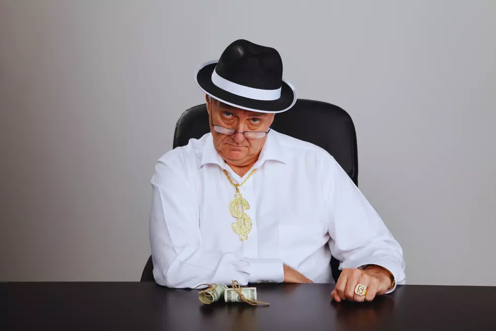 a sleazy looking pawnbroker with a gold dollar sign chain and rolled up money on his desk