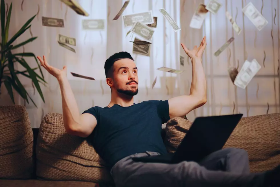 A man sits on the couch and throws dollar bills in the air