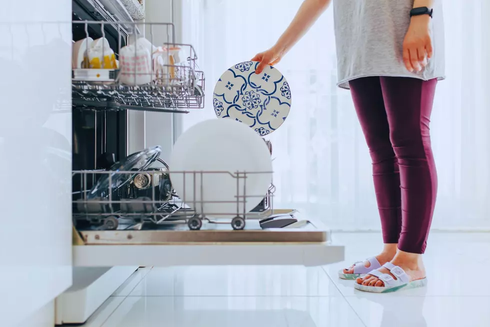 A woman in birkenstocks takes out a plate from the dishwasher