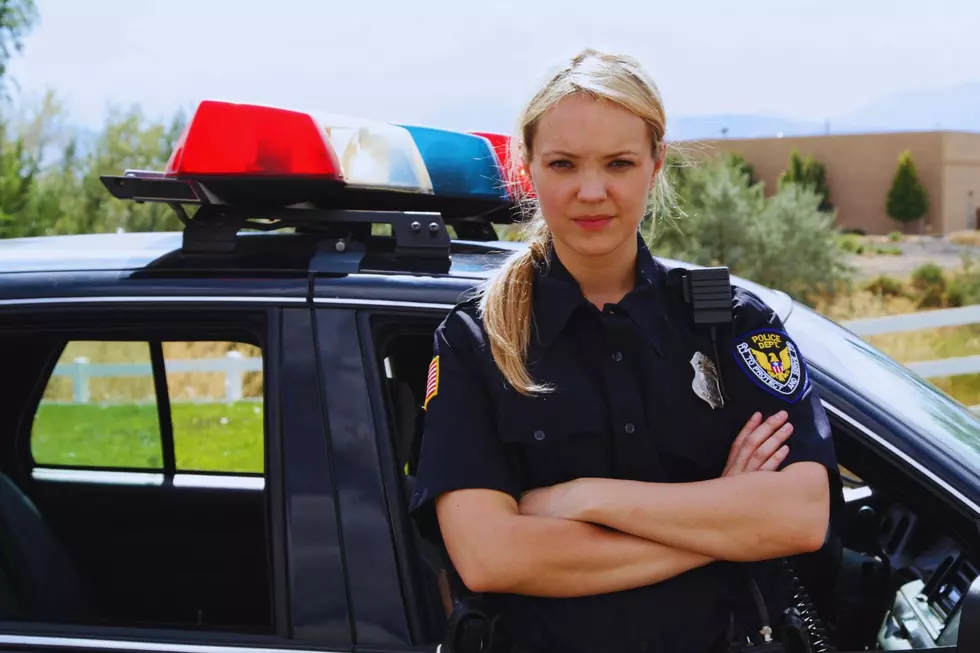 A female police officer with her arms crossed leans on her car