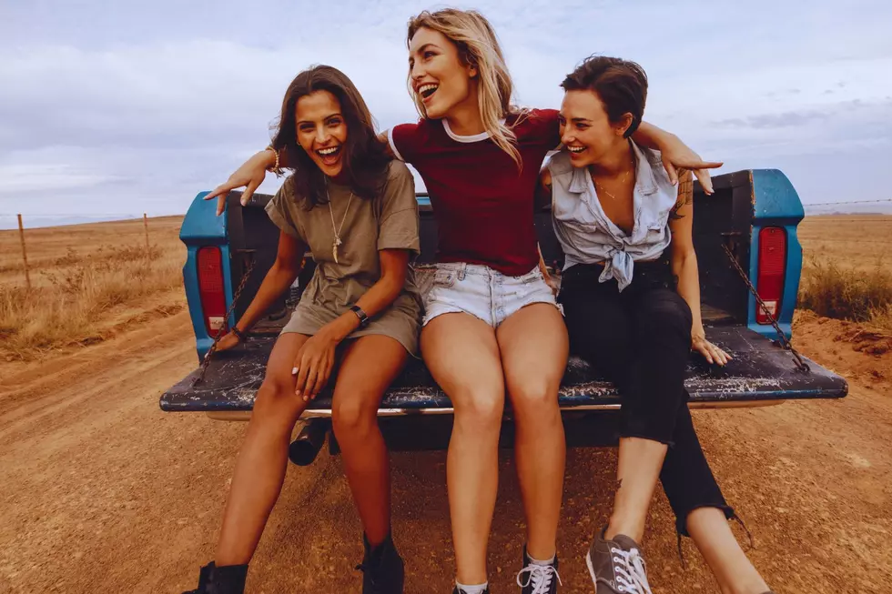 3 young women laughing while sitting on the tailgate of a pickup