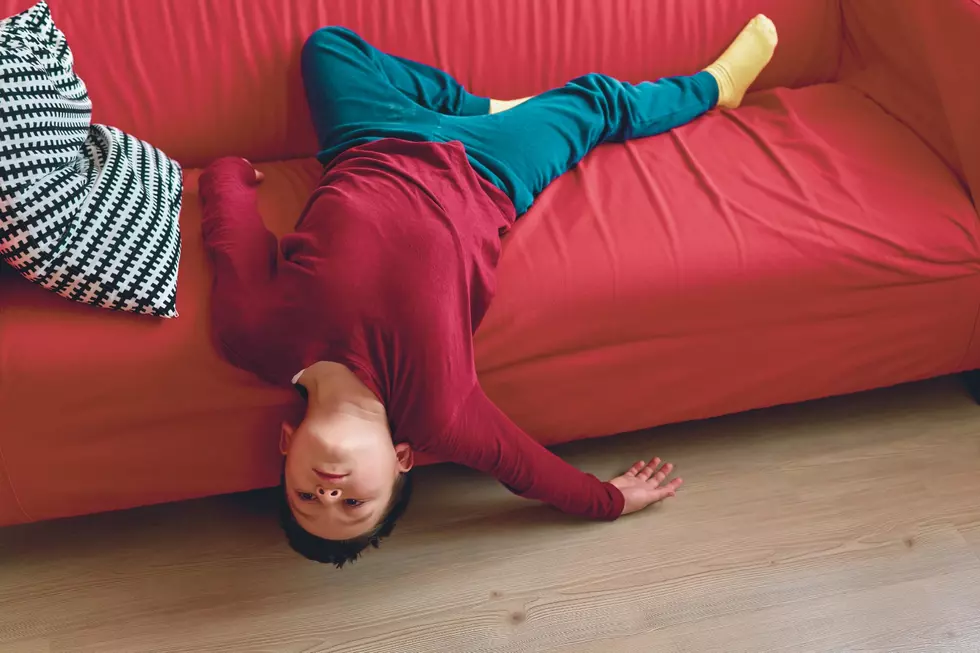 A kid looks bored while hanging upside down on a red couch