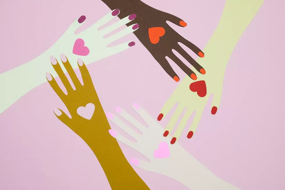 A drawing of 4 different hands all different races with hearts on them as they all 4 hold on to a wrist of another