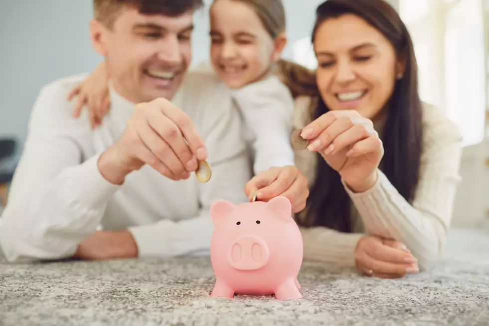 A family of 3 put money into a piggy bank while smiling