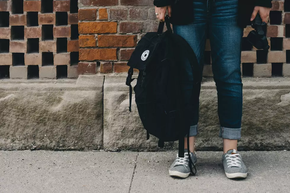 A girl holds a black backpack in one and headphones in another