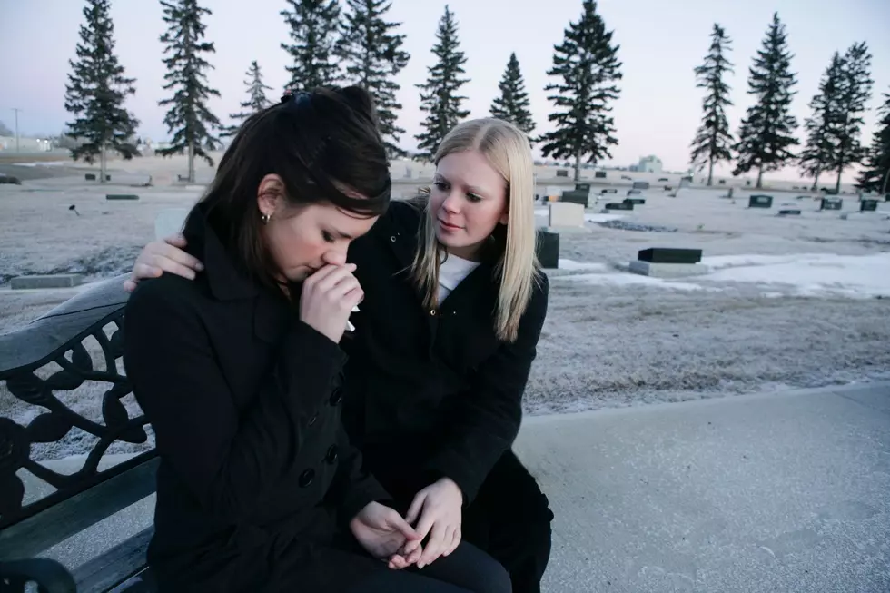 A woman consoles her crying friend after a funeral