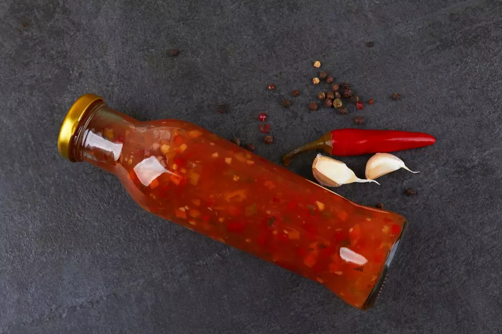 A bottle of hot sauce nesxt to a chili pepper and garlic cloves