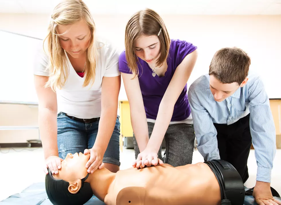 Students practicing CPR life saving techniques on a mannequin.