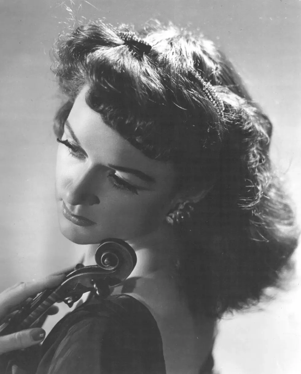 Black and white photo of a lady holding a violin with her head tilted.