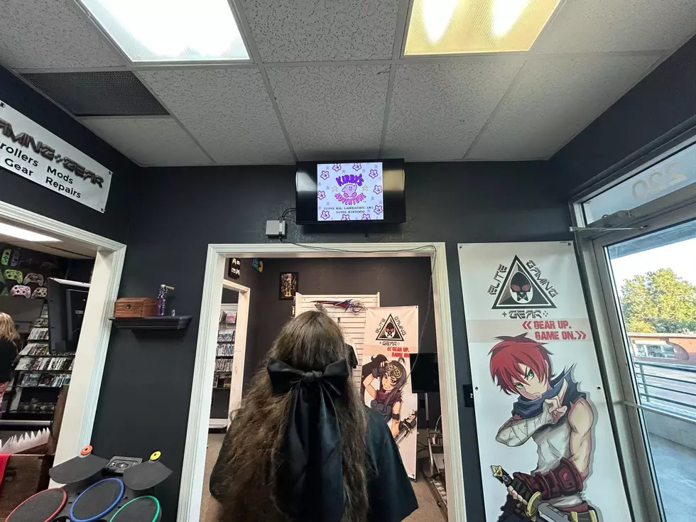 woman playing a video game, her back to us, video screen mounted above a doorway.