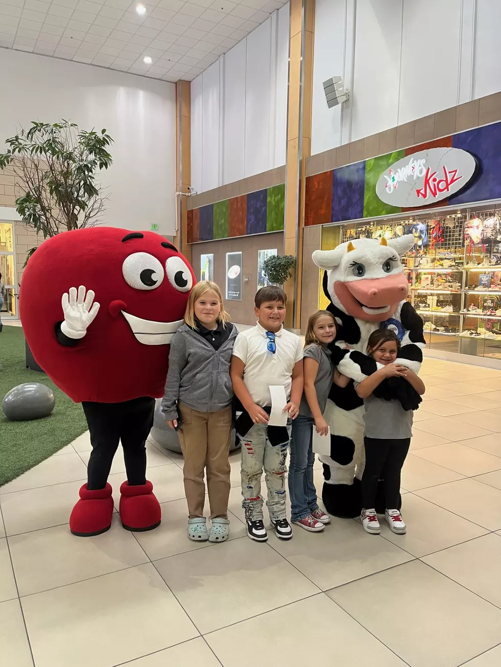 children next to fun mascots. A cow and an apple inside a mall