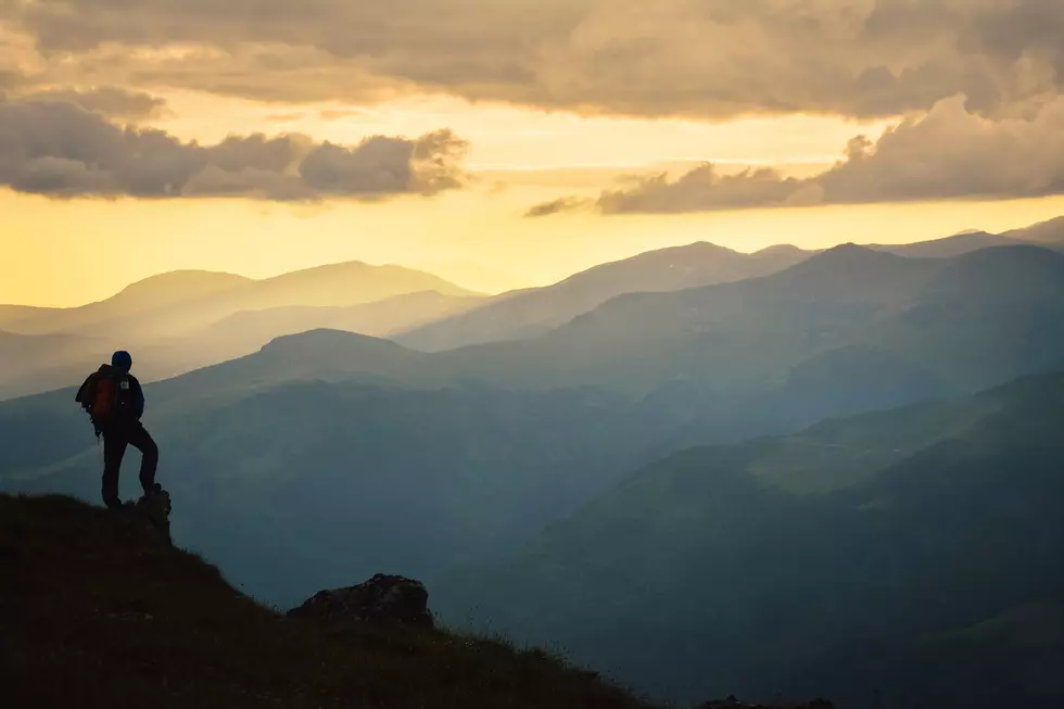 Hiker with backpack standing on top of a mountain cliff and enjoying sunset