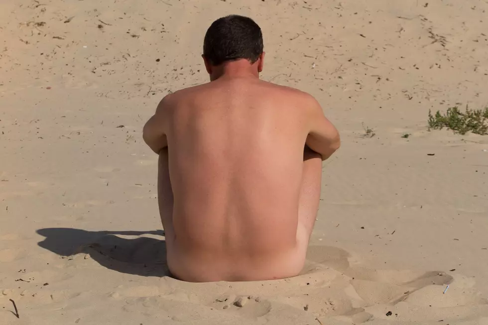 A naked man is sitting cross-legged on an empty beach and meditating.