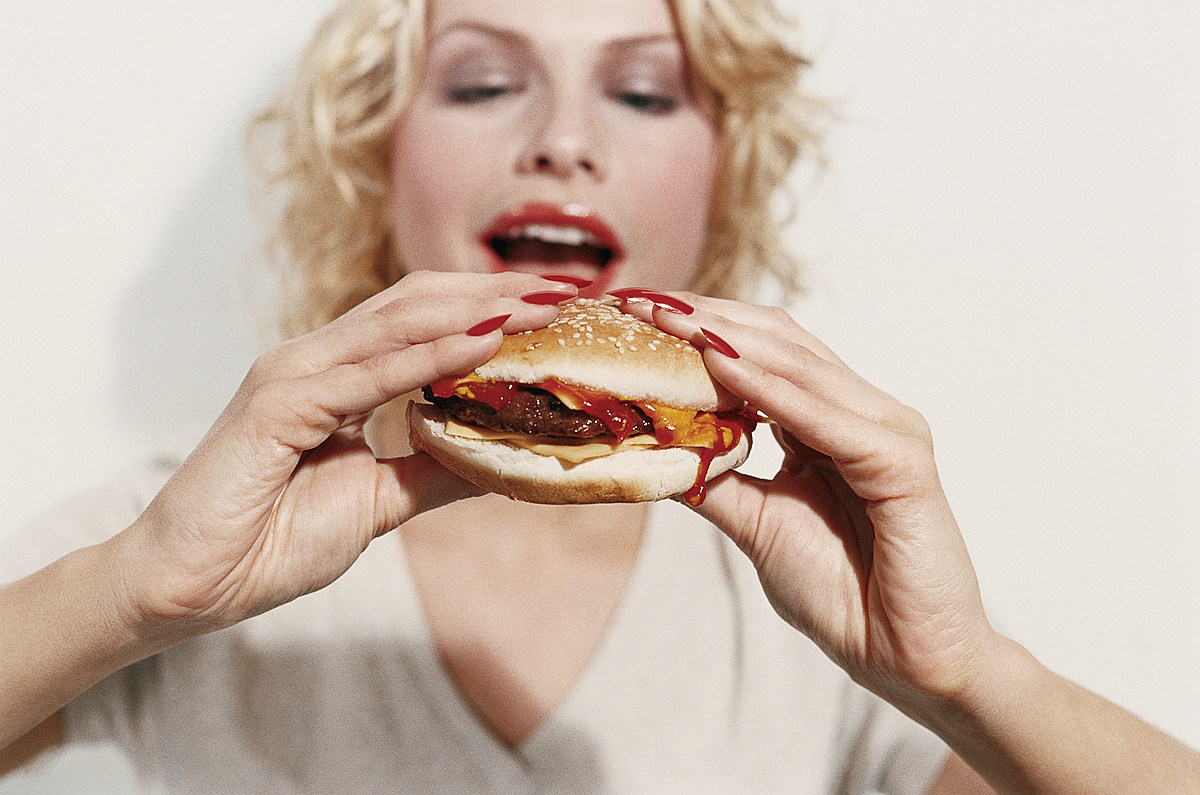 Боли во рту при приеме пищи. Девушка ест. Девушка ест гамбургер. Переедание. Еда на женщине.