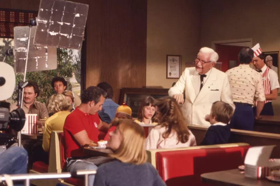 1970s photo of Colonel Sanders visiting a Kentucky Fried Chicken booth during a vintage commercial shoot in a classic fast-food restaurant.