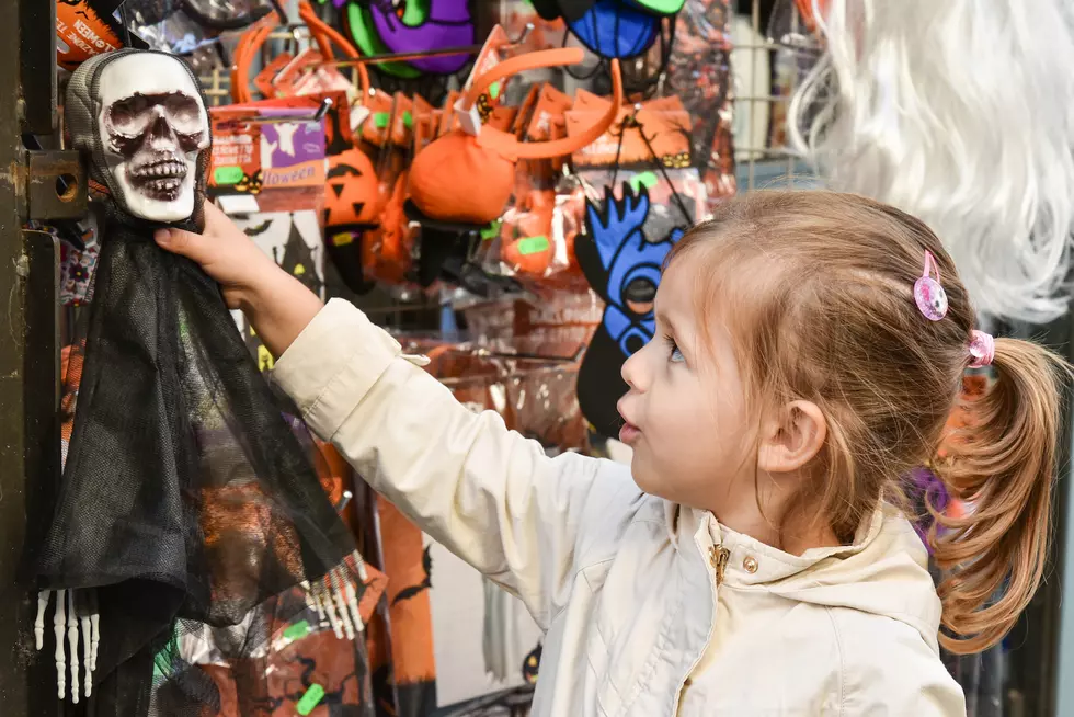 Cute little girl grabbing a skeleton in front of the shop during Halloween celebrations - Halloween business concept and consumerism concept