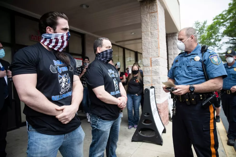 A police officer issues Atilis Gym co-owners Ian Smith, left, and Frank Trumbetti summons outside their gym in Bellmawr
