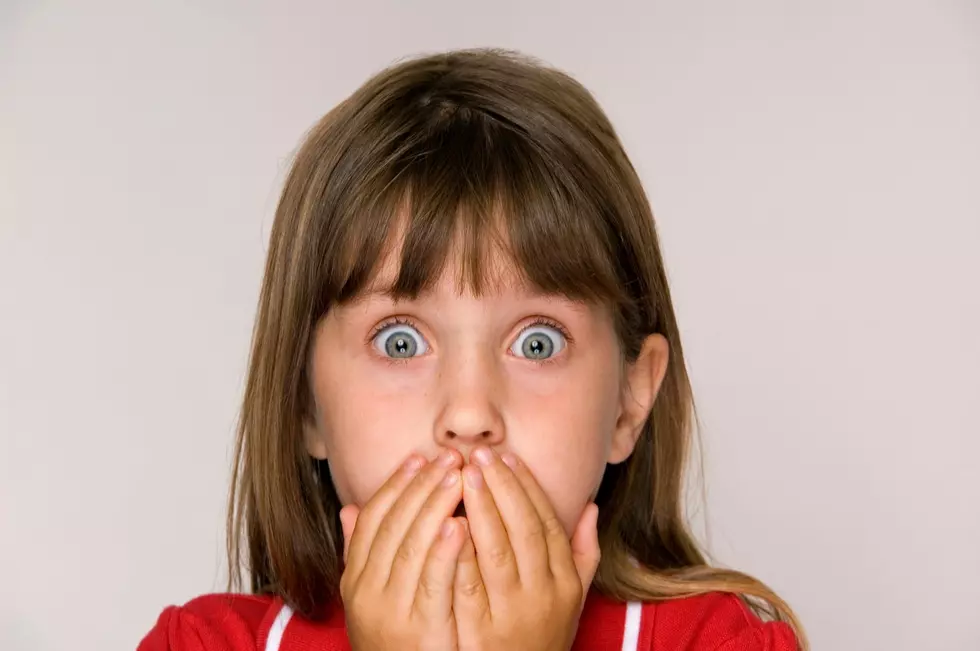 Scared six year old girl with hands covering mouth.