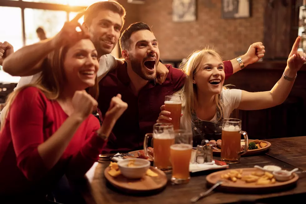 Happy friends cheering for their team while watching sports game on TV in a bar.