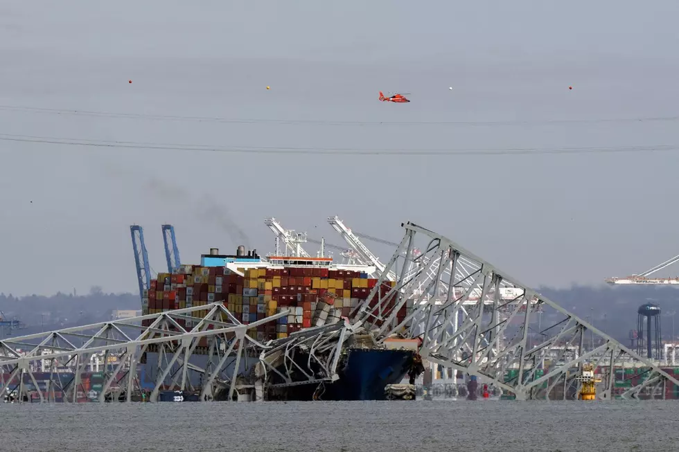 A helicopter flies over a container ship as it rests against wreckage of the Francis Scott Key Bridge on Tuesday, March 26, 2024, as seen from Pasadena, Md.
