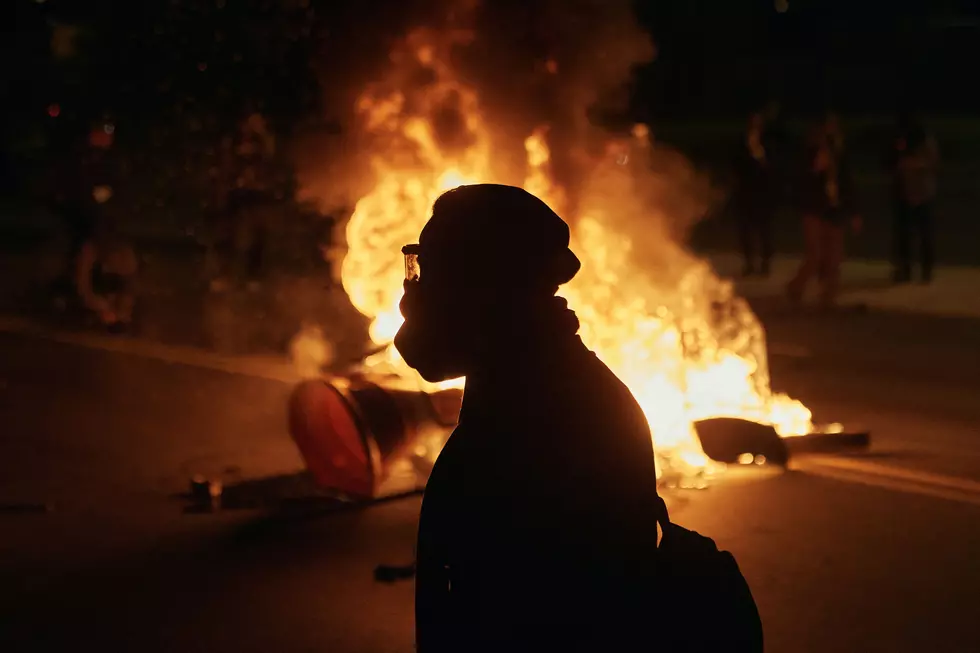 A man wearing protective gear walks in front of a burning barricade outside the Delaney Hall detention center during a protest against the transfer of detainees and federal immigration policies on Saturday, May 30, 2026, in Newark, N.J. (AP Photo/Andres Kudacki)