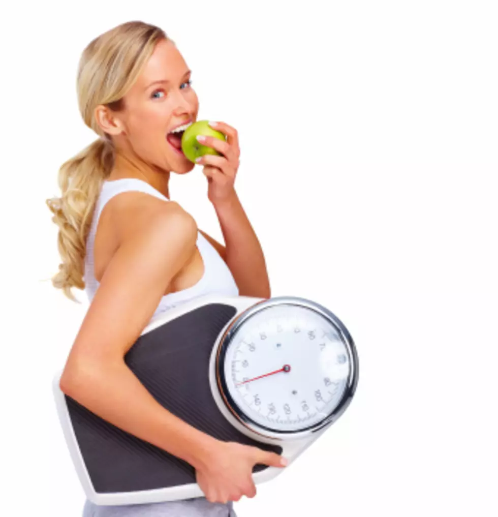 Young woman eating apple and carrying a weight scale over white background - Think Stock