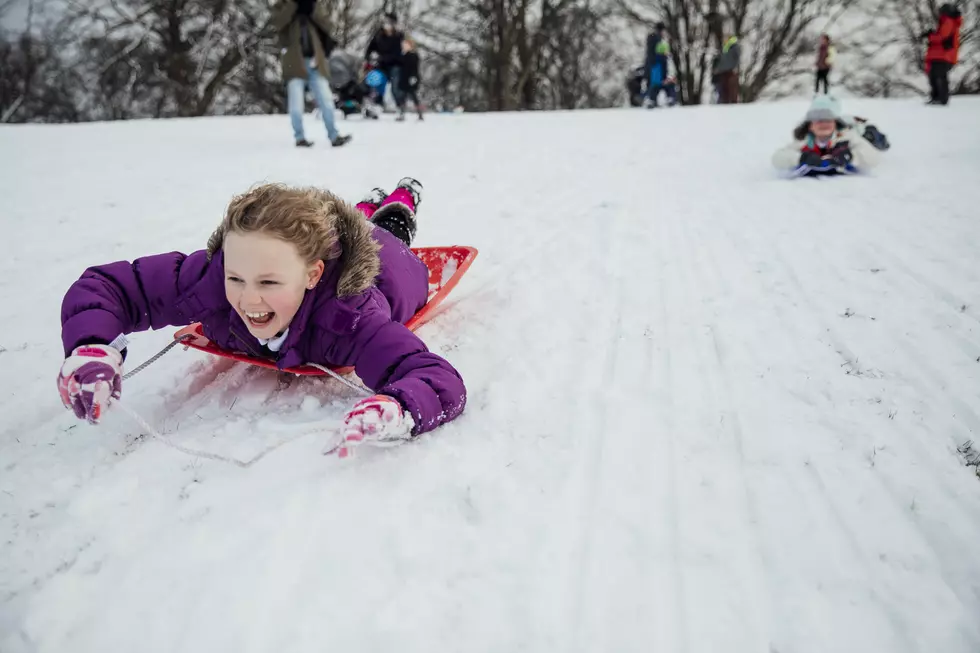 Little girl is lying on her belly on a sled, going down a big snowy hill in a public park.