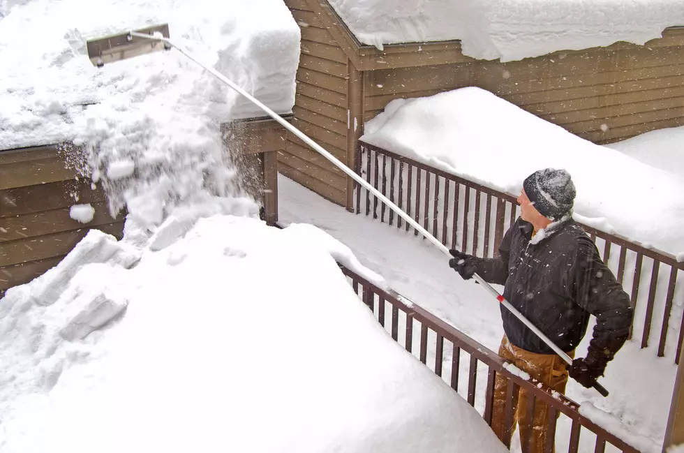 Man removing snow from a garage roof with rake.