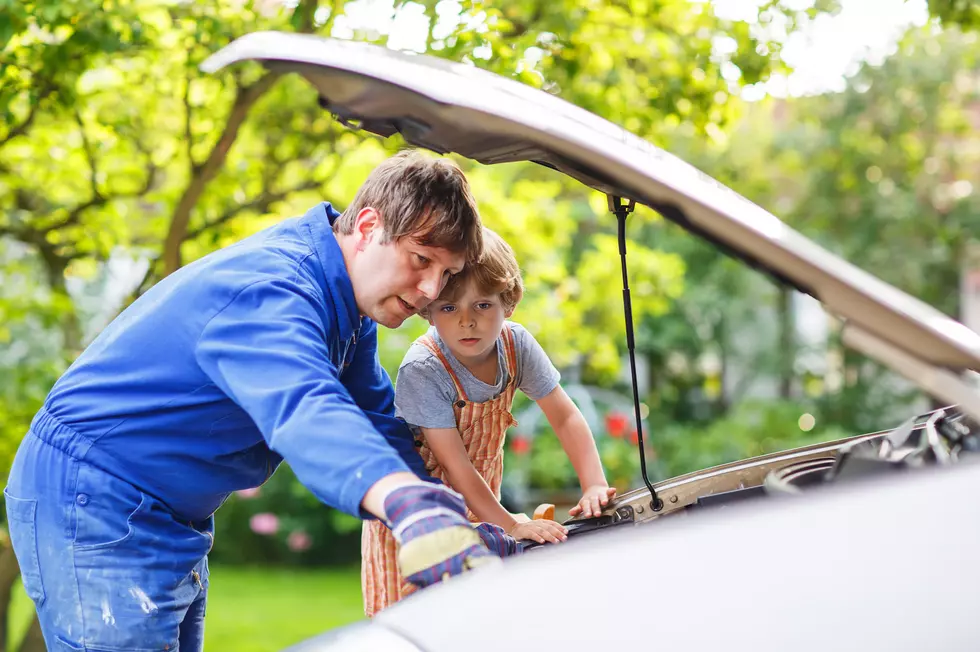 Young father teaching his little son to change motor oil in family car.