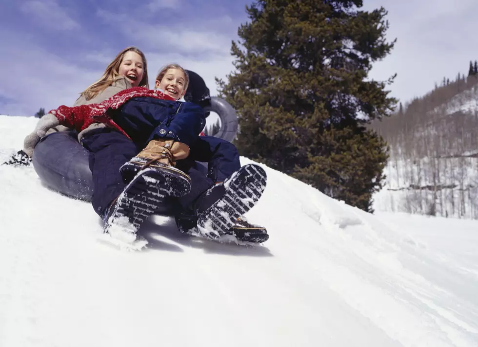 Girls (6-7) (12-13) sliding down snowy slope on inner tube, low angle view