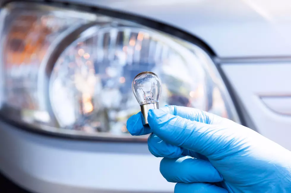 A hand holding a car light bulb, headlight in the background