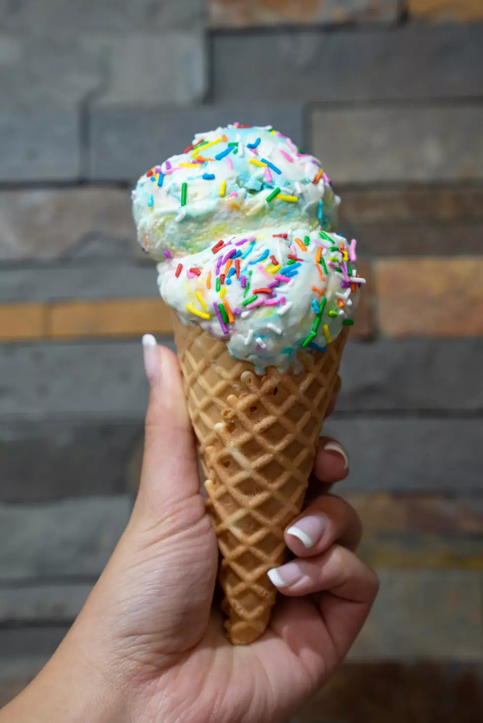 Womans hand holding waffle cone with birthday cake ice cream