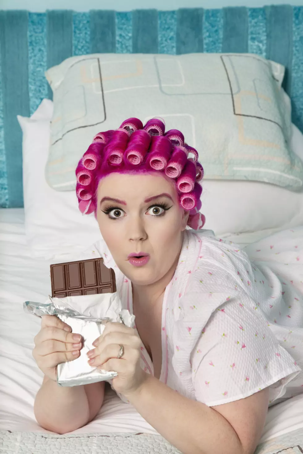 Portrait of shocked woman lying on bed with chocolate bar