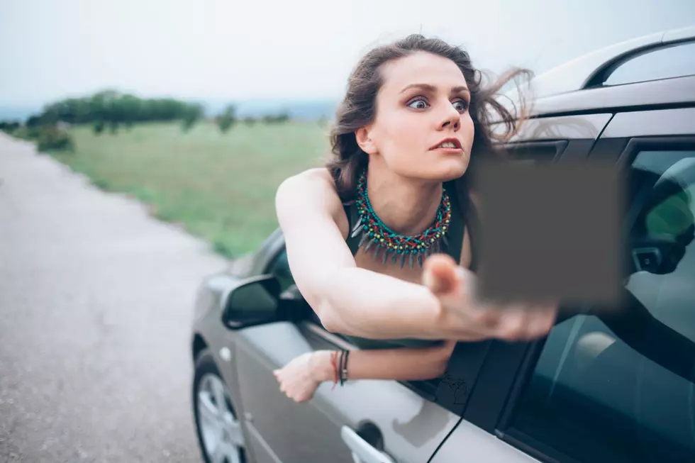 A woman leans out of her car to extend the middle finger