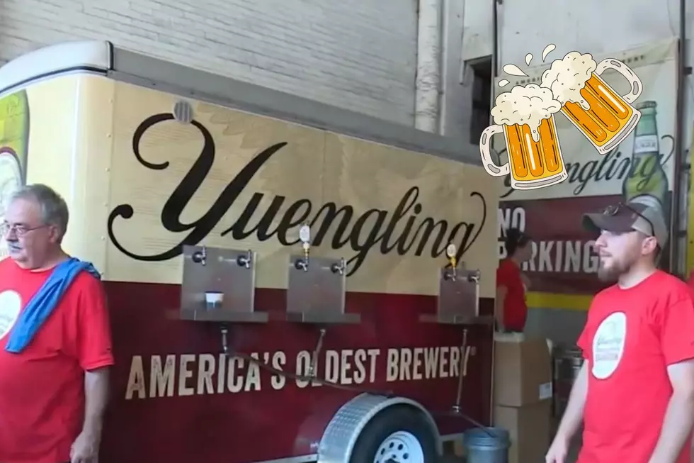 A Yuengling draft trailer is seen with two workers looking off to the left and two mugs full of beer clinging together.