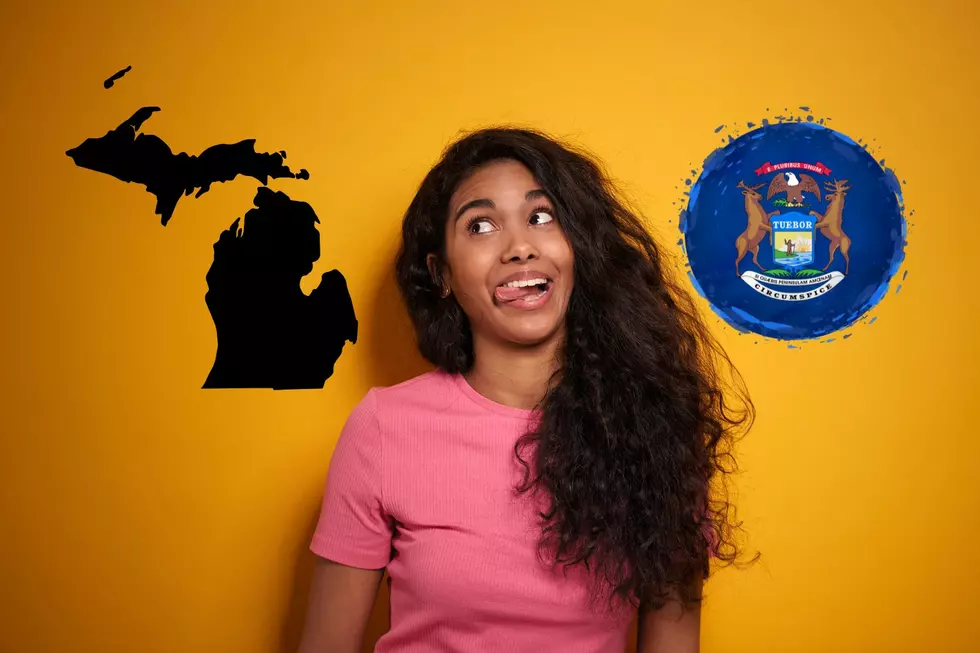 A woman leans against a wall with her tongue twisted while looking at an outline of Michigan.