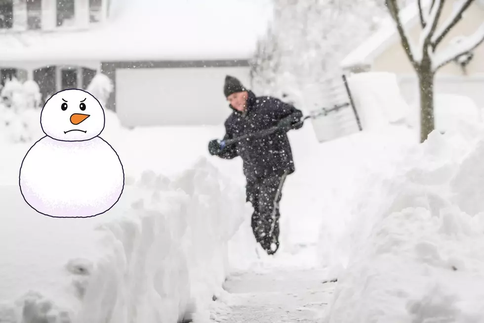 A man shovels a path in his driveway which is buried in three feet of snow. An angry cartoon snowman looks on in disapproval.