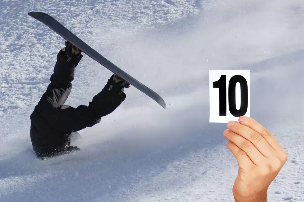 A snowboarder falls, appearing to be buried upside down in the snow with their feet and board in the air. A hand holding a card reading 10 is seen in the lower right hand corner.