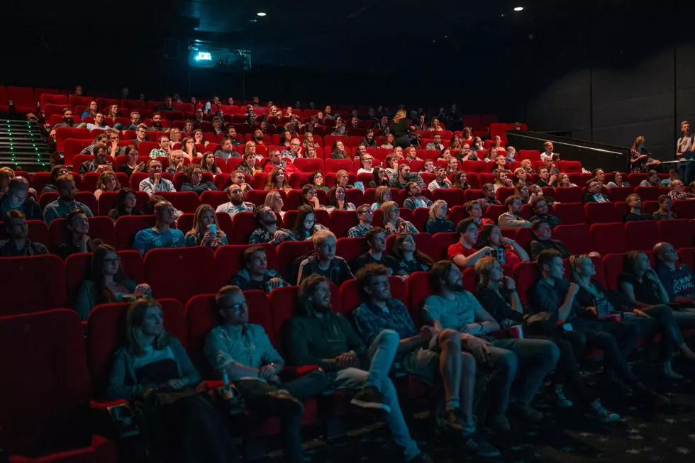 A movie theater packed with people with the lights still partially up as previews and commercials play before the film.