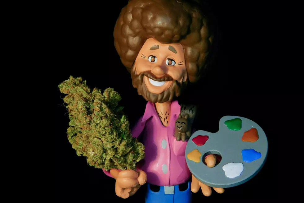 A miniature Bob Ross figurine is seen holding a marijuana bud and a pallet of paint.