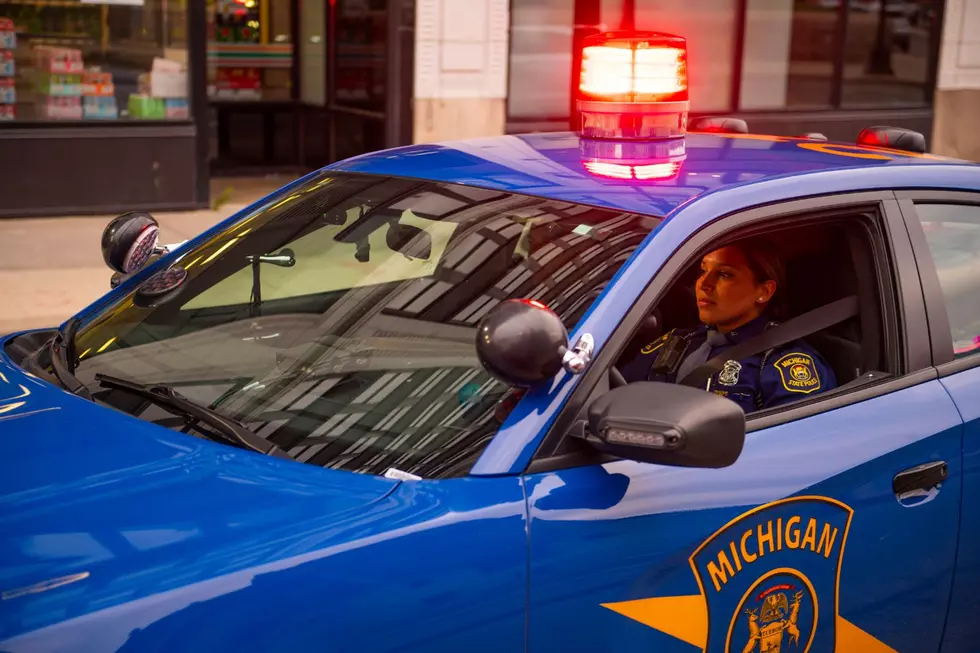 A trooper sits in a Michigan State Police cruiser with the red dome lit up.