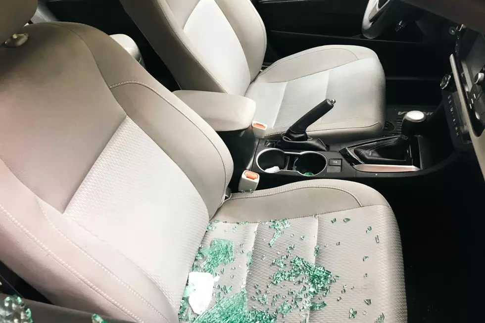 A car interior is seen with shattered glass on the seat and a broken window.