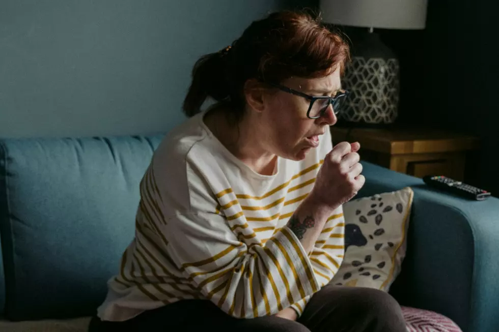 A woman sits on a couch, coughing into her hand.