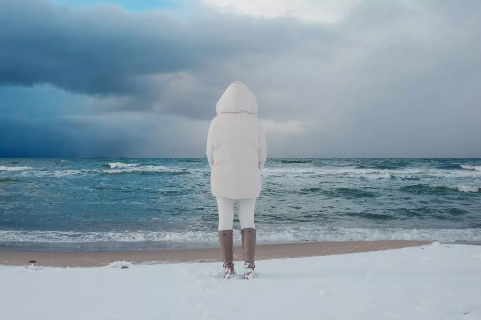 A woman stands by a snow covered lakeshore.