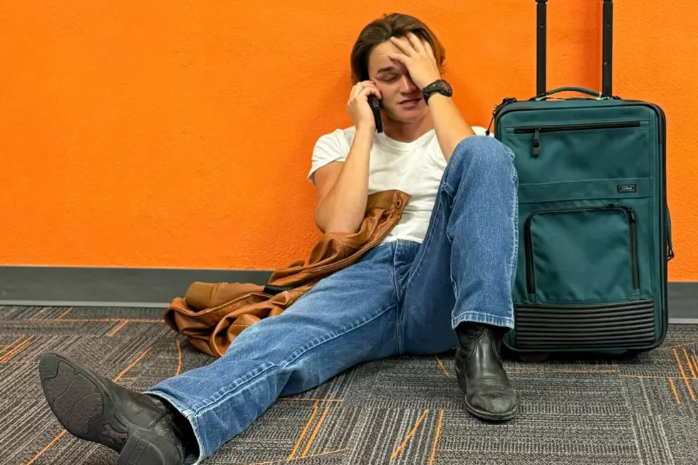 A man sits on the floor of an airport next to his luggage while talking on a cell phone.