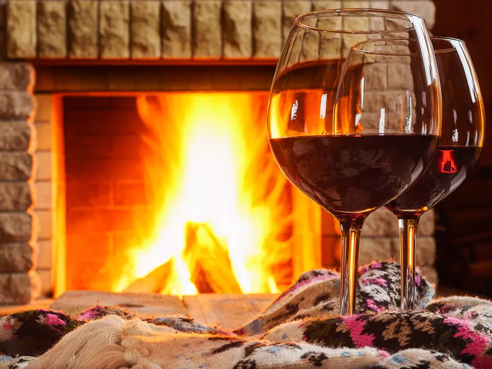 Two glasses of red wine and woolen things near cozy fireplace.