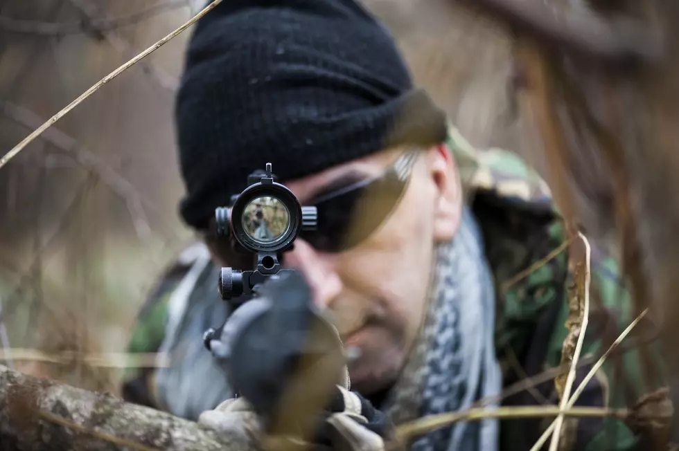 man laying in the weeds aiming a firearm