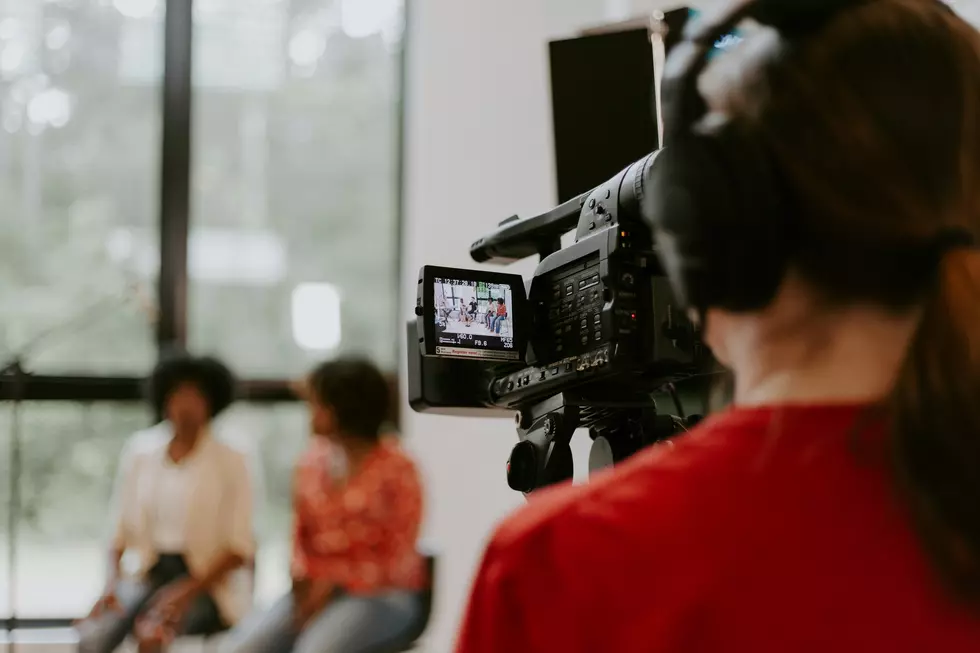 a woman behind a camera with headphones on filming people sitting and talking