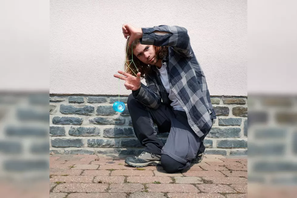 A Caucasian guy sitting on the ground outdoors, playing with a yoyo