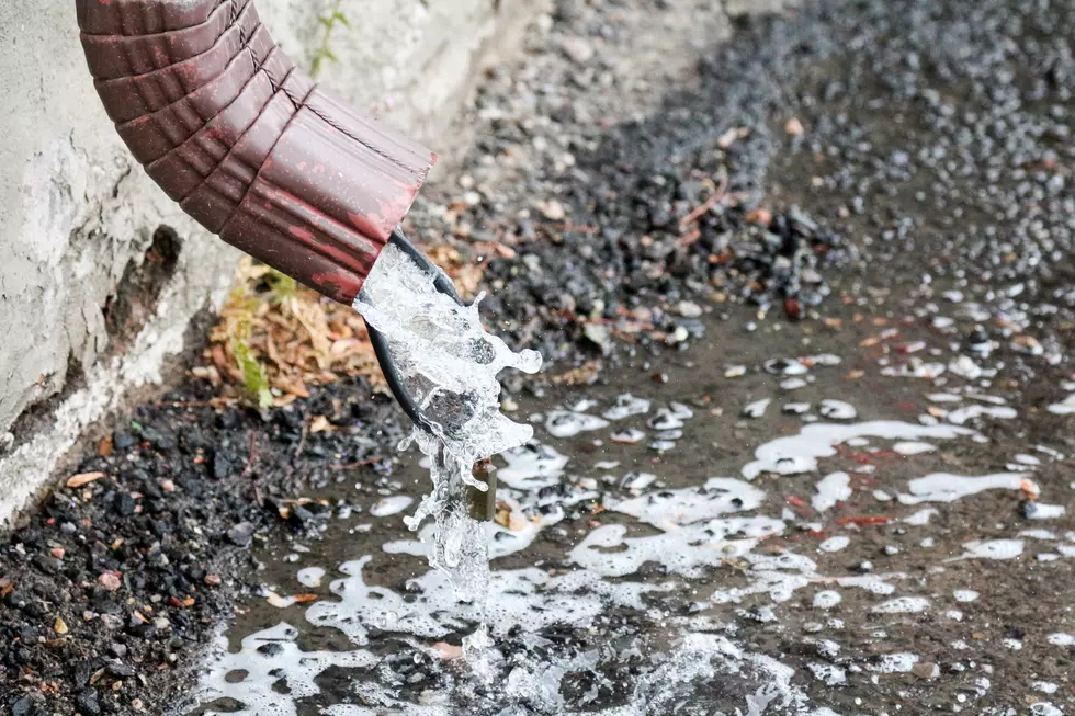 Rainwater gutter downspout with water pouring out onto cement